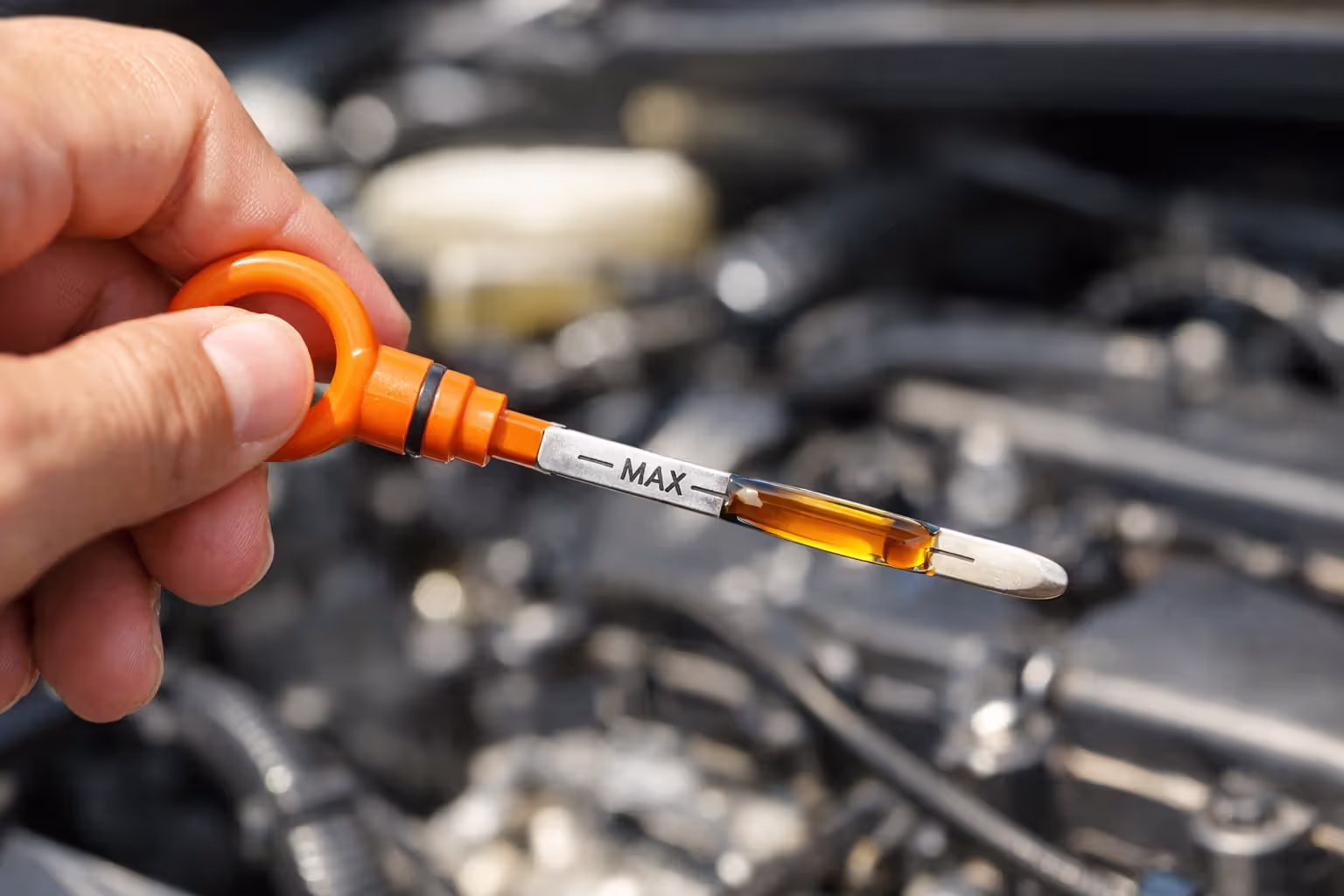 Close-up of hand pulling engine oil dipstick showing oil level between minimum and maximum marks