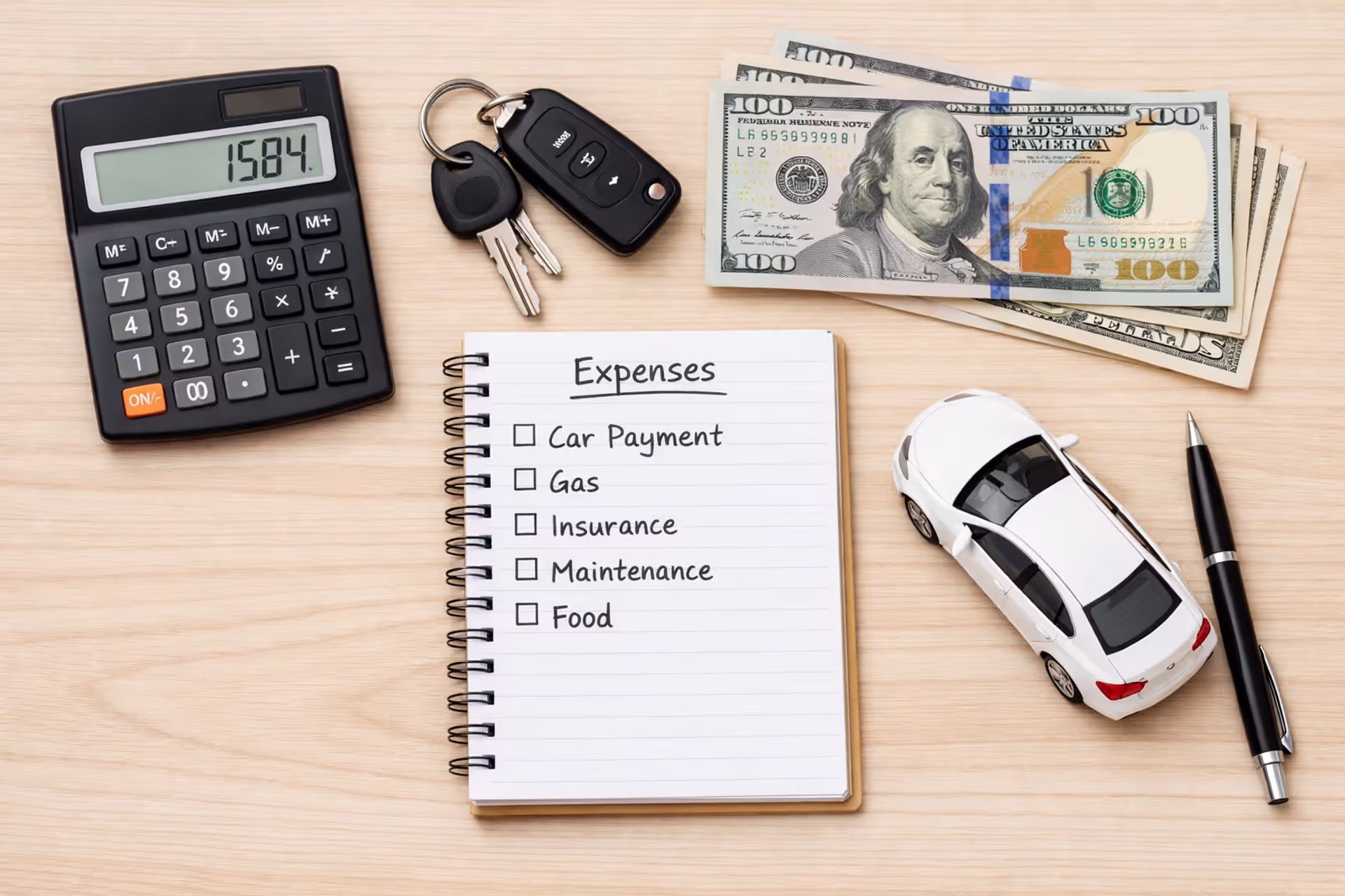 Flat lay of car keys, calculator, dollar bills, expense notebook, and miniature white sedan on wooden desk representing vehicle ownership cost planning